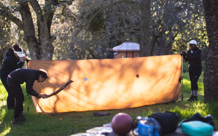 a group of people work together to set up a a tarp shelter on an outward bound course for bipoc